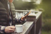 Чоловік п'є каву за допомогою цифрового планшета на балконі — стокове фото