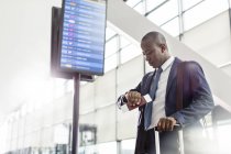 Бизнесмен проверяет время на наручных часах под табло вылета в аэропорту — стоковое фото