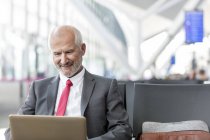Бізнесмен, який працює з ноутбуком у зоні відправлення аеропорту — стокове фото
