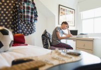 Gitarre liegt vor gelangweiltem Jungen bei Hausaufgaben am Schreibtisch im Schlafzimmer — Stockfoto