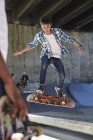 Enfocado adolescente volteando monopatín en el parque de skate - foto de stock