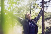 Donna esuberante escursionismo sorridente con le braccia alzate e la testa indietro nel bosco soleggiato — Foto stock