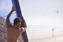 Homem levantando kiteboarding pipa na praia ensolarada — Fotografia de Stock