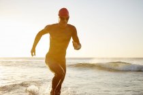 Male triathlete swimmer in wet suit running from ocean — Stock Photo