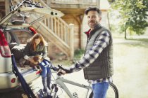 Portrait smiling man with mountain bike near car behind cabin — Stock Photo