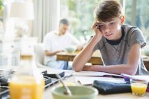 Frustrated boy doing homework at breakfast — Stock Photo
