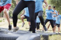 Des personnes déterminées sautant des pneus sur le parcours d'obstacles du camp d'entraînement — Photo de stock