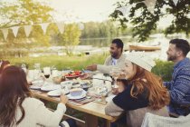 Друзья, наслаждающиеся обедом за столом на берегу озера — стоковое фото