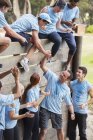 Teamkollegen helfen sich auf Boot-Camp-Hindernisparcours gegenseitig über Mauer — Stockfoto