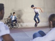 Friends watching teenage boy flipping skateboard at skate park — Stock Photo