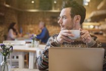Pensive man looking away drinking coffee at laptop in cafe — Stock Photo