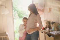 Porträt lächelnde Tochter mit schwangerer Mutter im Kinderzimmer — Stockfoto