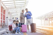 Family with suitcases waiting at train station platform — Stock Photo