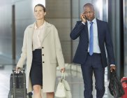 Business people walking with luggage in airport concourse — Stock Photo