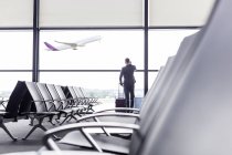 Бизнесмен с чемоданом разговаривает по мобильному телефону у окна зоны вылета из аэропорта — стоковое фото