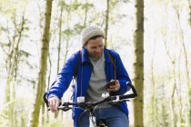 Man mountain biking texting with cell phone in woods — Stock Photo