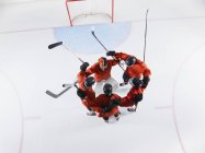 Overhead view hockey team in red uniforms huddling on ice — Stock Photo