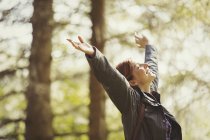 Exuberant woman hiking in sunny woods with head back and arms raised — Stock Photo