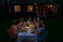 Семья наслаждается ужином при свечах за столом во внутреннем дворике возле дома ночью — стоковое фото