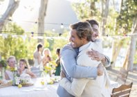 Жених и шафер обнимаются во время свадебного приема в домашнем саду — стоковое фото