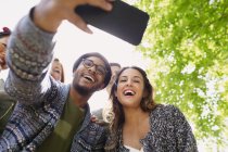 Enthusiastic friends taking selfie with camera phone below tree — Stock Photo