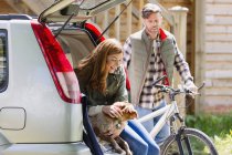 Couple with dog and mountain bike at back of car outside cabin — Stock Photo