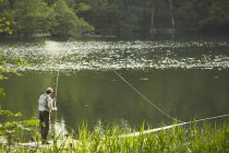Старший чоловік летить на риболовлю на літній річці — стокове фото