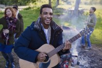 Retrato sorridente homem tocando guitarra com amigos no acampamento — Fotografia de Stock