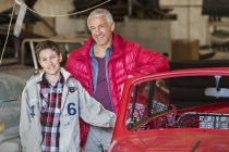 Retrato sorrindo pai e filho ao lado do carro clássico na oficina de reparação automóvel — Fotografia de Stock