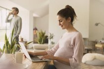 Pregnant woman using laptop at dining table — Stock Photo