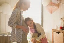 Daughter listening to pregnant mother?s stomach in nursery — Stock Photo