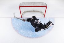 Overhead view hockey goalie reaching to block puck at goal net — Stock Photo