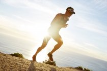 Corredor de triatleta masculino corriendo a lo largo del océano - foto de stock