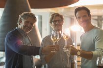 Портрет улыбающихся мужчин, пьющих белое вино на винодельне — стоковое фото