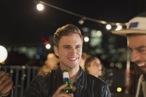 Улыбающийся молодой человек пьет пиво на вечеринке на крыше — стоковое фото