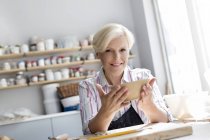 Portrait smiling mature woman holding bowl in pottery studio — Stock Photo