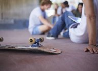 Skateboard upside-down next to teenage friends hanging out at skate park — Stock Photo