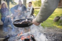 Man cooking hot dogs over campfire for friends — Stock Photo
