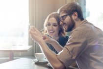 Пара, использующая мобильный телефон в солнечном кафе — стоковое фото