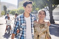 Sonriente pareja de adolescentes caminando por la soleada calle urbana - foto de stock