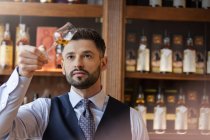 Grave barista ben vestito esaminando whisky — Foto stock