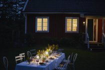 Вечеринка при свечах на свечах, ужин снаружи освещенного дома ночью — стоковое фото
