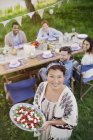 Retrato sorrindo mulher servindo salada Caprese para amigos na mesa de festa do jardim — Fotografia de Stock