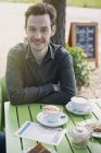 Portrait smiling man enjoying cappuccino at outdoor cafe table — Stock Photo