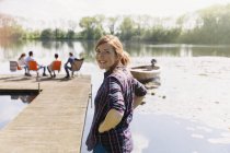 Retrato mulher sorridente na ensolarada doca à beira do lago — Fotografia de Stock