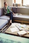 Творческая предпринимательница рассматривает доказательства и разговаривает по мобильному телефону на офисном диване — стоковое фото