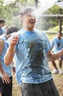 Enthusiastic man enjoying water hose spray on boot camp obstacle course — Stock Photo