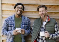 Portrait smiling men drinking coffee outside cabin — Stock Photo