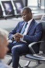 Businessman checking the time on wristwatch waiting in airport departure area — Stock Photo