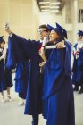 College graduates in cap and gown with diplomas taking selfie — Stock Photo